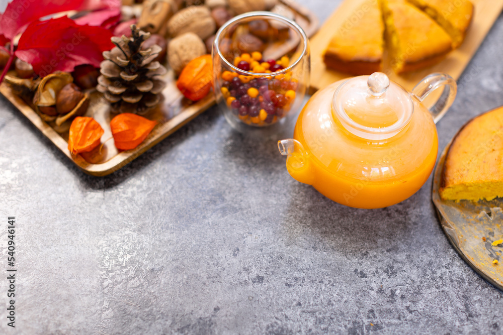 A glass teapot with a beautiful orange pie drink on a gray table. Beautiful background with pumpkin pie and berry tea on the kitchen table with copy space. A glass teapot with a beautiful orange pie drink on a gray table. Beautiful background with pumpkin pie and berry tea on the kitchen table with copy space.
