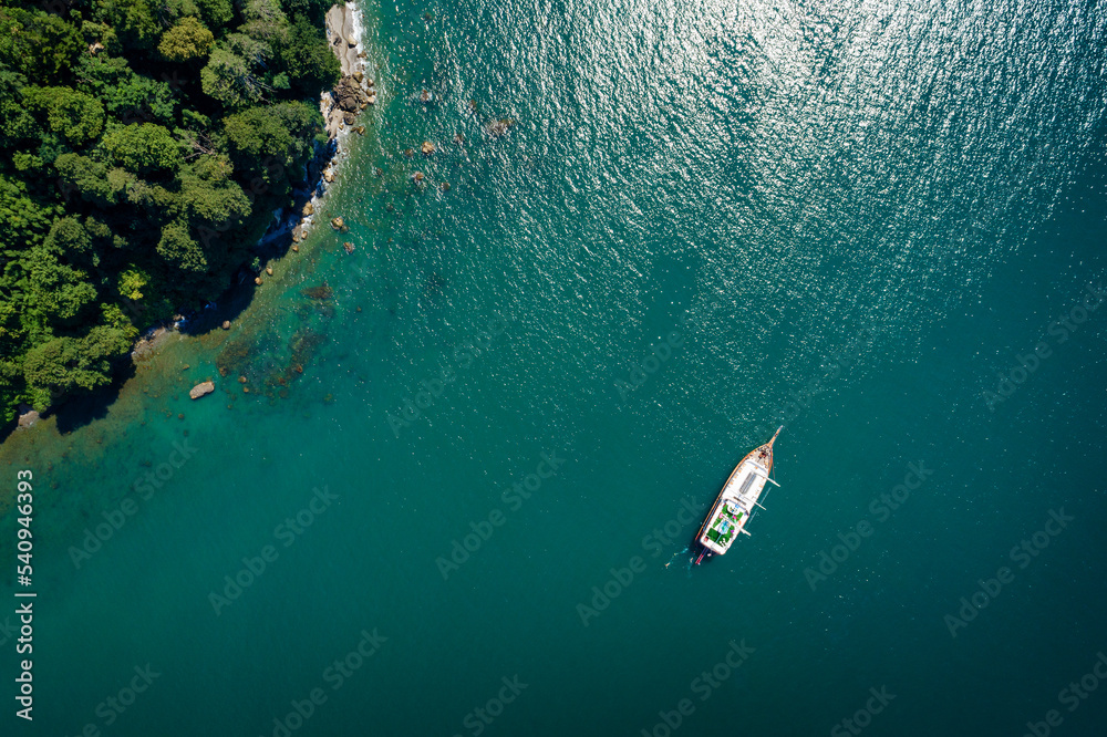 Top view of a sailboat anchored off a rocky coast