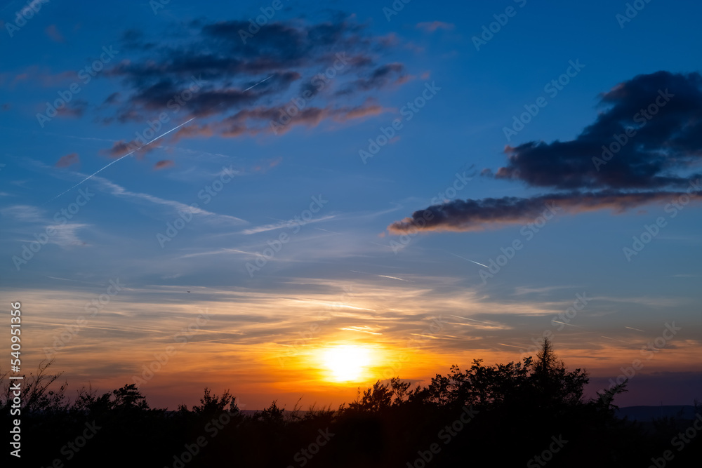 Sunset panorama above Sauerland forest treetops with romantic view over Ruhr Basin Germany. Colorful sky with aircrafts and evening clouds on a summer day seen from viewing point Danzturm Iserlohn.