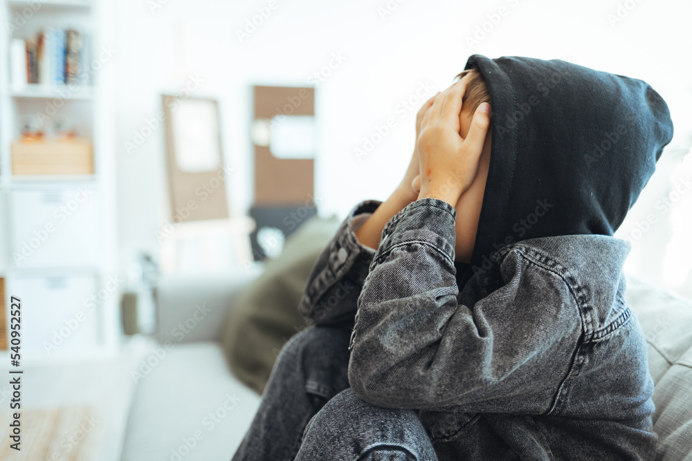 Young preteen teenager boy holding his had in his bedroom with smartphone, Cyber bullying in kid, depressed child mental health, fomo, social distancing concept. Lonely sad boy at home Young preteen teenager boy holding his had in his bedroom with smartphone, Cyber bullying in kid, depressed child mental health, fomo, social distancing concept. Lonely sad boy at home