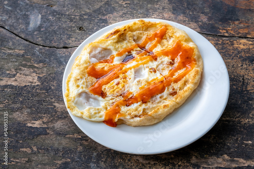 Fried roti with egg on white plate and wooden table.