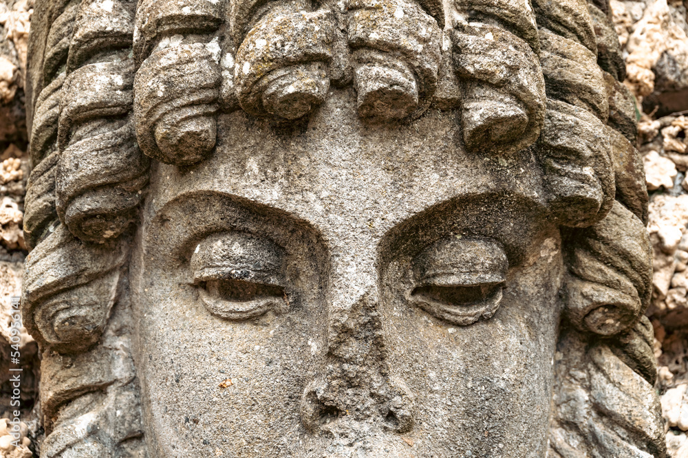 Part of the face of an ancient stone statue with incredibly beautiful and expressive eyes and curls around the face