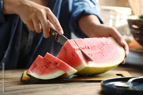 Woman cutting fresh juicy watermelon at wooden table, closeup