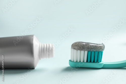 Brush with charcoal toothpaste and tube on light background  closeup