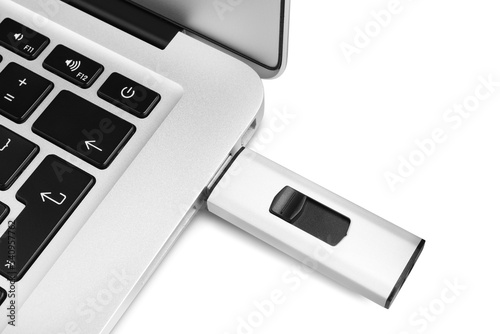 Modern usb flash drive attached into laptop on white background, top view photo