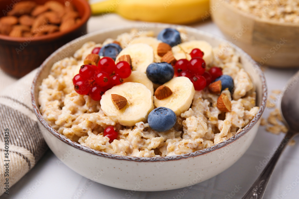 Oatmeal served with berries, almonds and banana slices on white table, closeup Oatmeal served with berries, almonds and banana slices on white table, closeup