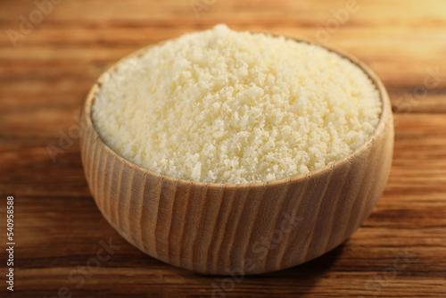 Bowl with grated parmesan cheese on wooden table, closeup
