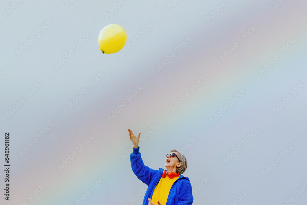 modern style dressed older lady playing with a balloon with raised arm on rainbow background modern style dressed older lady playing with a balloon with raised arm on rainbow background