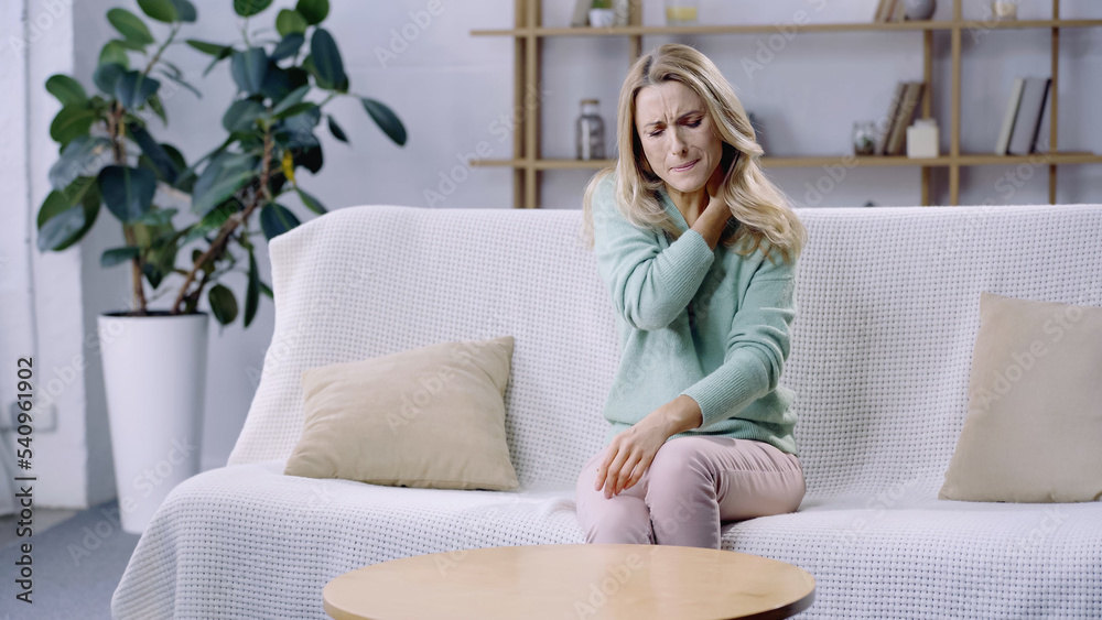 blonde woman with closed eyes having pain in neck while sitting on sofa blonde woman with closed eyes having pain in neck while sitting on sofa