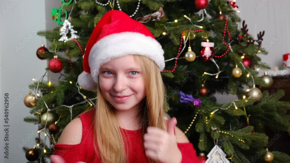 Pretty girl in red Santa's hat dancing near the New Year tree. Christmas and New Year concept Pretty girl in red Santa's hat dancing near the New Year tree. Christmas and New Year concept