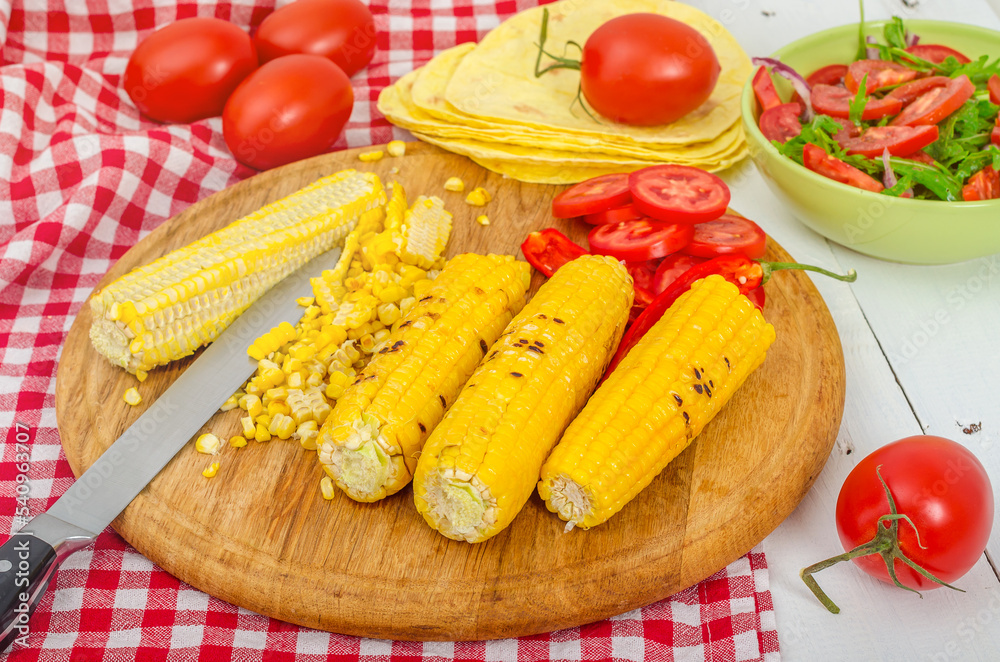 Hot grilled corn with tomatoes on kitchen table