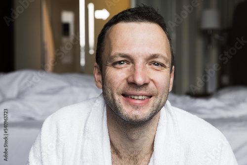 Happy young adult man in white cotton bathrobe