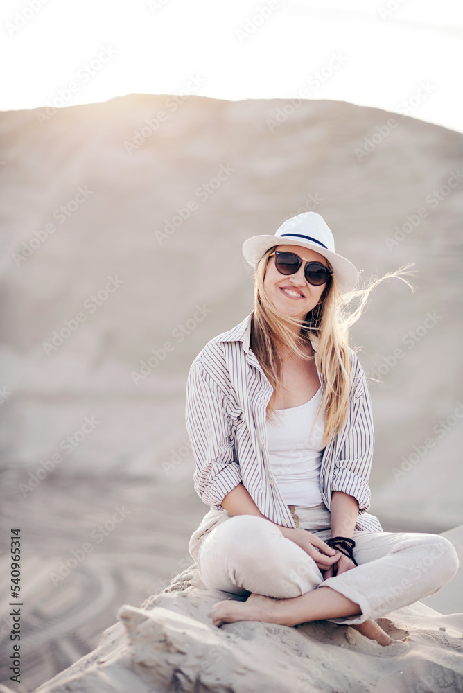 stylish happy attractive smiling woman posing in desert sand dressed in white clothes with hat at sunset, vacation safari, sunny summer day stylish happy attractive smiling woman posing in desert sand dressed in white clothes with hat at sunset, vacation safari, sunny summer day