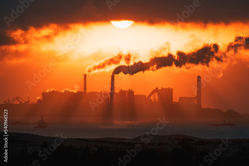 thermoelectric chimneys expel steam or smoke in a fiery sunset on the ocean s shore