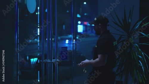 Guard or security worker walking , closing door and turning  plate with open closed sign at night . Guard dressed security uniform working inside storage or shop . Concept of night shift work