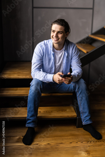 Young man sitting on stair and using mobile phone at home