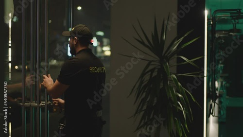Guard or security worker walking , closing door and turning  plate with open closed sign at night . Guard dressed security uniform working inside storage or shop . Concept of night shift work