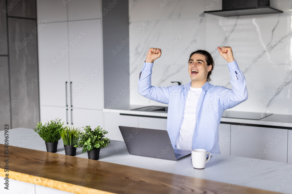 Excited young man winner sit at home table looking at laptop screen celebrating online success victory euphoric overjoyed by internet sport bet win got new job opportunity or loan approval in email