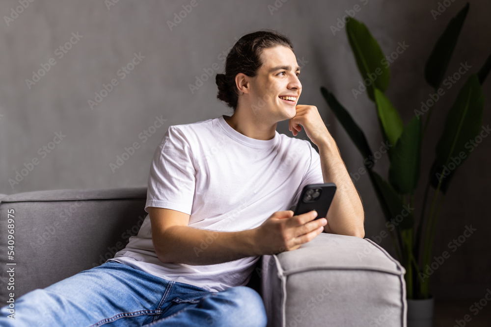 Happy man relax on couch at home chatting with friends on smartphone. Excited male writing message on cell to girlfriend. Smiling guy using mobile phone texting or playing app games Happy man relax on couch at home chatting with friends on smartphone. Excited male writing message on cell to girlfriend. Smiling guy using mobile phone texting or playing app games