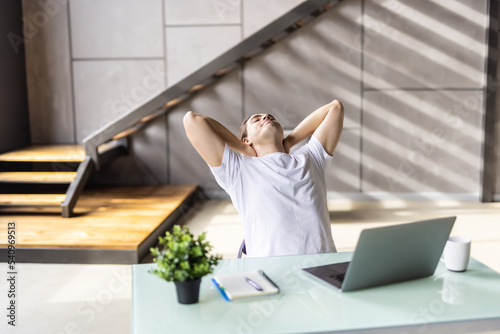 Meeting friday. Happy young guy freelancer enjoy calm moment when task is done relax rest stretch back hold hands over head. Serene millennial man recline on chair with closed eyes take break in work