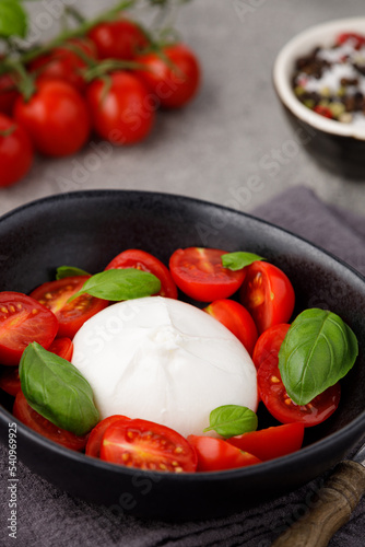 Burrata cheese with tomatoes and basil in a plate on a gray stone kitchen table, top view. Burrata cheese ball made from mozzarella and cream. Italian cuisine