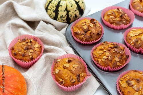 Homemade pumpkin muffins with pumpkin seeds and walnut pieces. Fall baking for Thanksgiving and Halloween. Cupcakes in baking dish on linen napkin. Selective focus. Top view. Close up