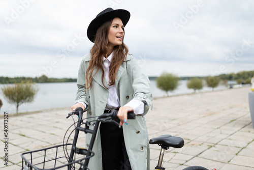 stylish young girl with a bicycle in a black hat on the embankment