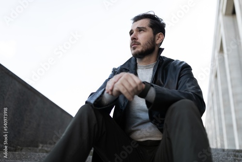 a man on the street sits on the steps in depression with prostration looks into the distance