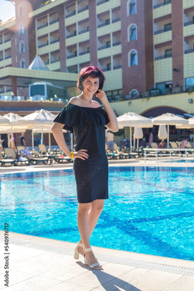 Portrait of a woman in a black dress by the pool of a European hotel.