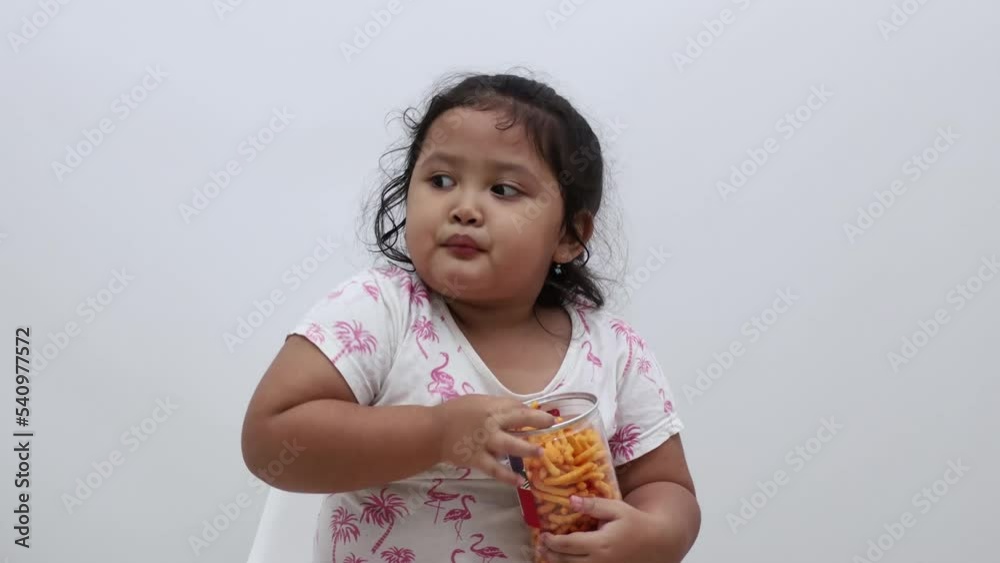 Happy asian little girl sitting while enjoying her snack. Isolated on white background Happy asian little girl sitting while enjoying her snack. Isolated on white background
