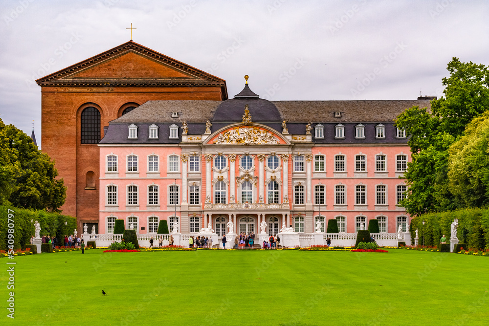 Naklejka premium Famous view of the Electoral Palace in Trier, Germany with the basilica behind it. The lawn and flower beds in front of the main entrance to the south wing are bordered by hedges and trees.