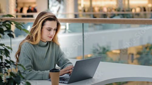 Caucasian business female freelancer student designer worker sitting at table in cafe office corporate space working with laptop typing message drinking coffee tea e-learning online shopping free wifi