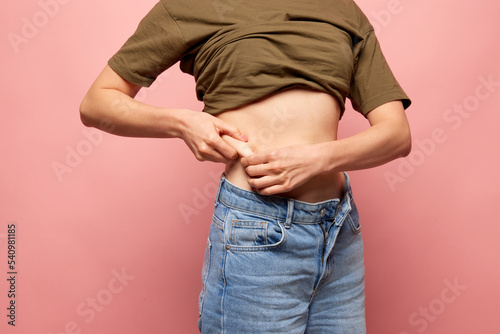 Closeup female hands stretching skin on her belly, model showing to camera her abdomen. Concept of dieting, sport, fitness, healthy lifestyle, body positive and wellbeing
