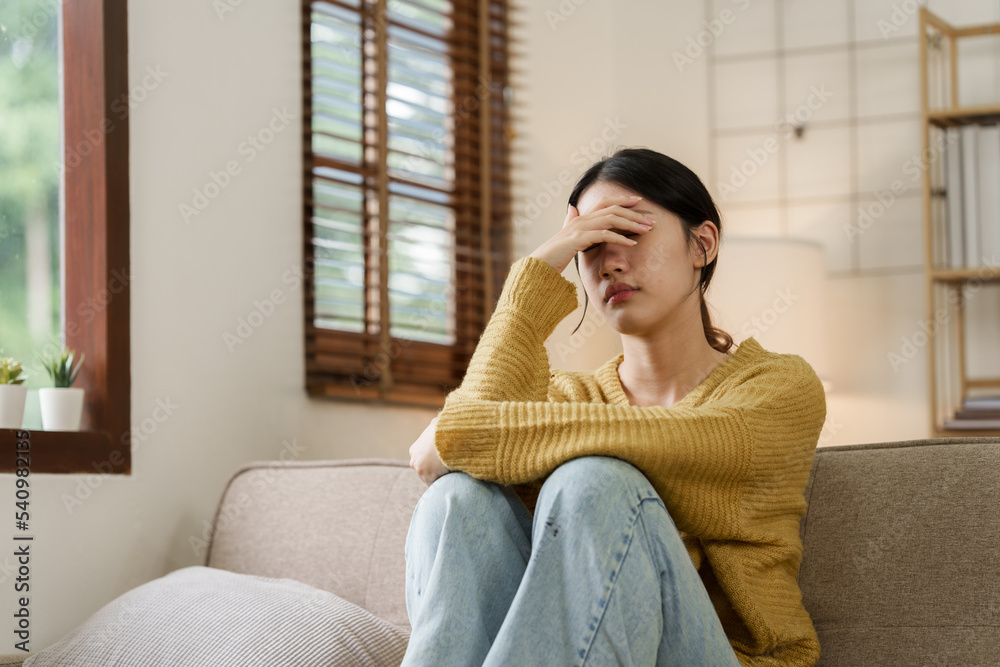 Asian woman with a headache and stress while sitting on the sofa at home Asian woman with a headache and stress while sitting on the sofa at home