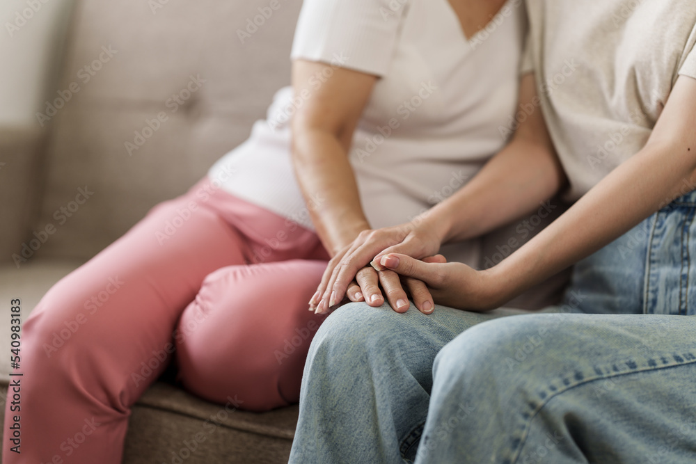Elderly mother and grown daughter holding hands sitting on the sofa To show love, encouragement and concern