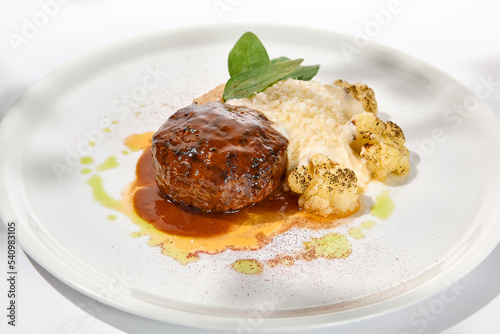 Beef cutlet with grilled cauliflower with gravy and cheese sauce on white plate. Elegant beefsteak on light background with shadows of sunlight. Summer menu with hard shadows Meat ball of minced meat