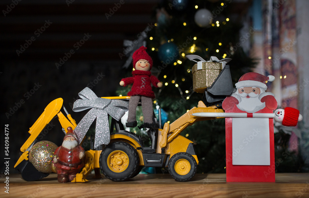 concept of new year business greetings in construction company. toy bulldozer - excavator, souvenir Santa Claus, festive notebook with place for advertising inscription on background of Christmas tree