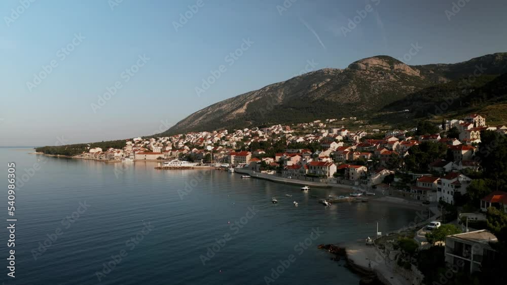 The sun rises over the small town of Brac on the island of Bol, Croatia. The town is situated on a steep hillside overlooking the Adriatic Sea. The footage is shot from the above sea, giving a bird's The sun rises over the small town of Brac on the island of Bol, Croatia. The town is situated on a steep hillside overlooking the Adriatic Sea. The footage is shot from the above sea, giving a bird's