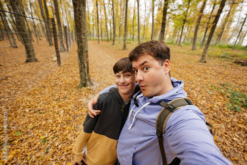 Son with father making selfie with funny faces in autumn forest.