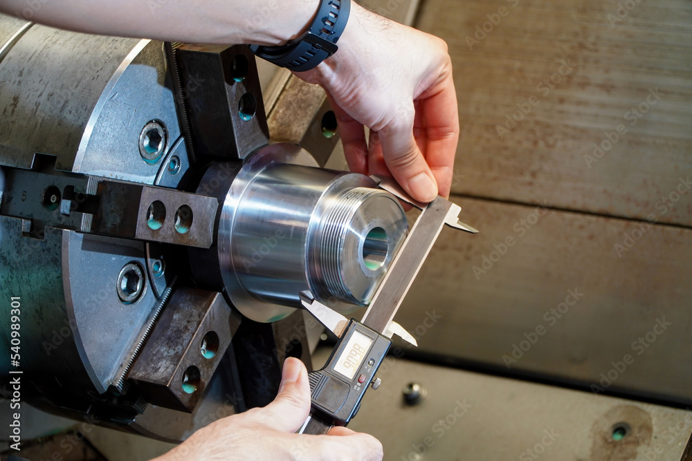 Hands of an engineer measures a metal part with a digital vernier caliper. Quality control of part machined on a lathe,Quality control concept of Qc.