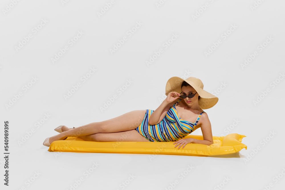 Portrait of young beautiful woman in stylish swimming suit lying on inflatable mattress isolated over white background