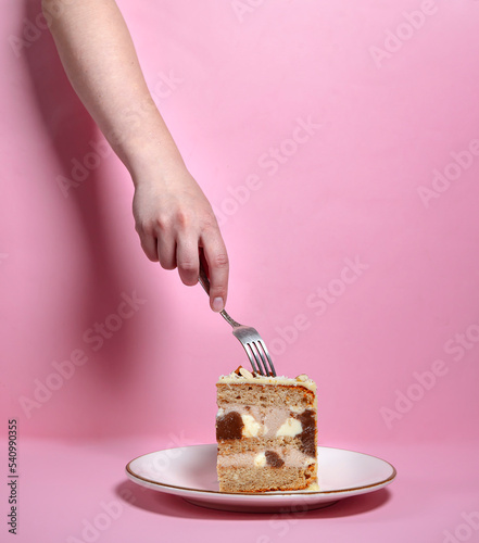 The girl's hand wants to taste a piece of cake on a plate in white chocolate, decorated with nuts, cookies and chocolate. on a pink background. exclusive offers. copy space. confectionery advertising