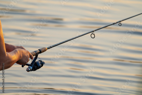 telescopic fishing rod with inertia reel in men's hands on the background of river water
