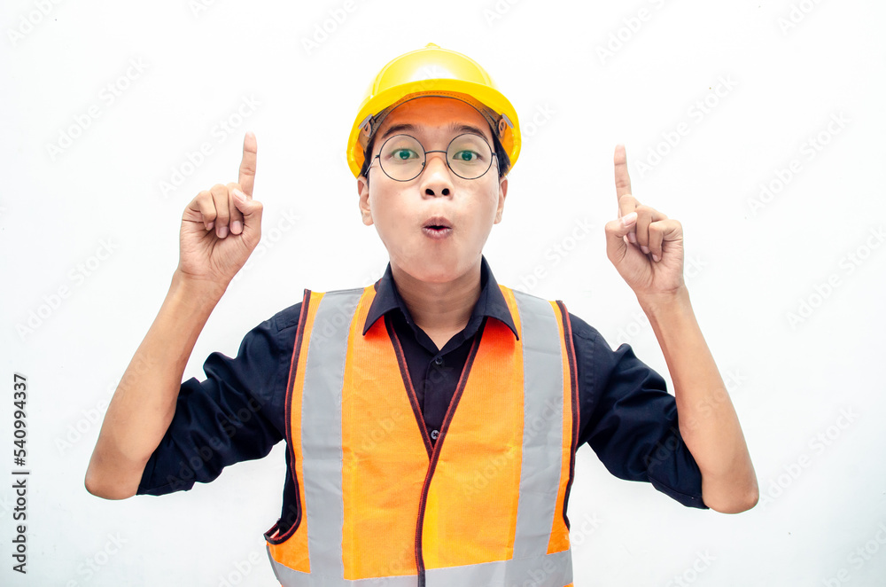 young asian consrtruction worker wearing yellow safety helmet and orange vest smiling and pointing finger with happy and shocked expression. billboard model advertisment concept.