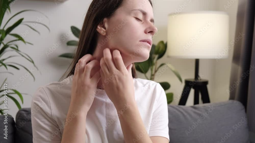 Close up of sad young woman sitting on couch chair scratching neck has