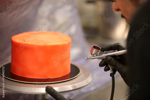 pastry chef designer using edible red paint airbrush to spray frosted cup cake photo