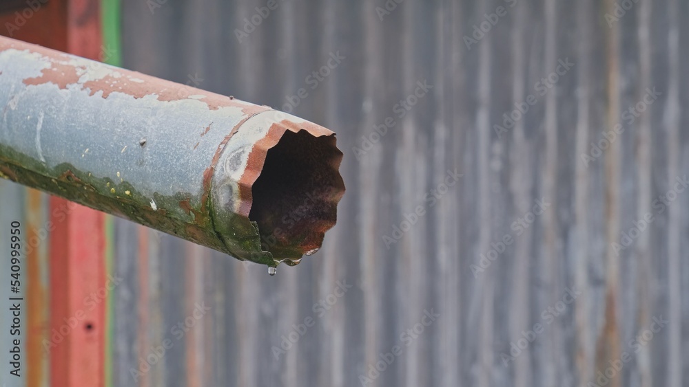 Water Drops of Rainwater Dripping from Old Rusty Roof Metal Gutter