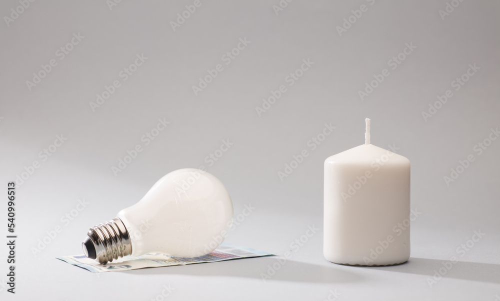 white candle and light bulb on top of 20 euro banknotes, gray background white candle and light bulb on top of 20 euro banknotes, gray background