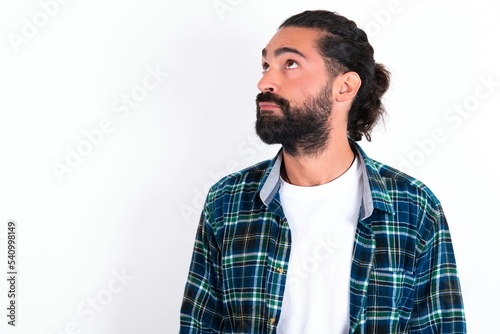 young bearded hispanic man wearing plaid shirt over white background , looks pensively aside, plans actions after university, imagines what to do Thinks over about new project.