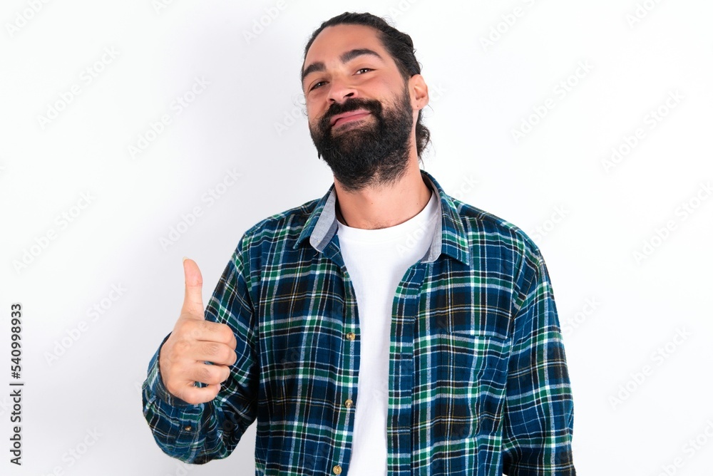 young bearded hispanic man wearing plaid shirt over white background giving thumb up gesture, good Job! Positive human emotion facial expression body language. young bearded hispanic man wearing plaid shirt over white background giving thumb up gesture, good Job! Positive human emotion facial expression body language.